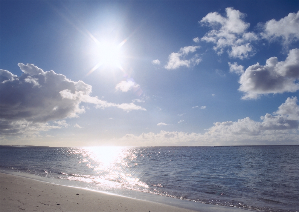IMAGE_この写真は、明るい太陽と青い空、そして穏やかな海が写っている風景です。雲が浮かび、海面には日光が反射している様子が見えます。これはおそらくビーチや海岸の風景を表現したものです。リラックスできる自然の景色ですね。