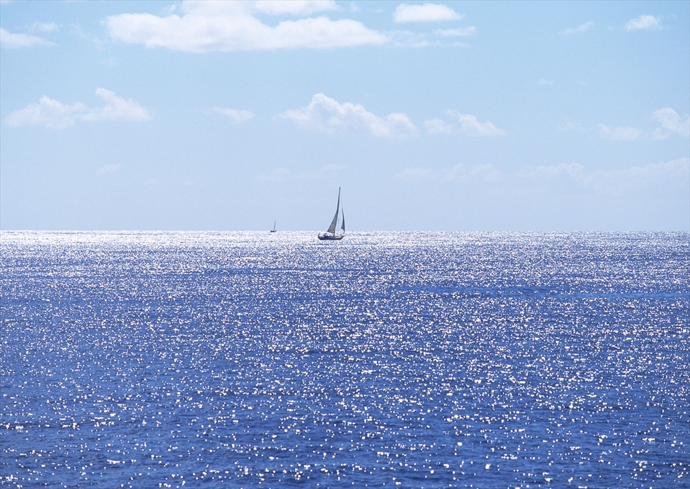 IMAGE_この写真は、青い海と太陽の光が反射してキラキラと輝いている様子が写っており、いくつかの帆船が遠くに見えます。全体として、穏やかで美しい海の風景を捉えたものです。