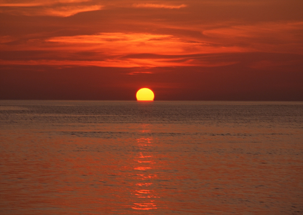 IMAGE_これは夕日が海の上に沈んでいる写真です。空はオレンジや赤の色合いで彩られており、静かな海面に反射しています。夕日の景色は一般的に美しく、自然の中でリラックスしたり、感動したりする瞬間を捉えています。