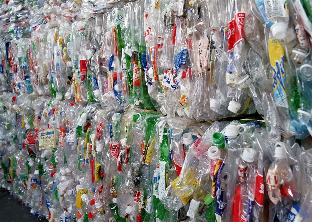 IMAGE_この写真は、リサイクルされたプラスチックボトルや容器が積み上げられている様子を示しています。プラスチック廃棄物の処理や再利用に関連していると考えられます。