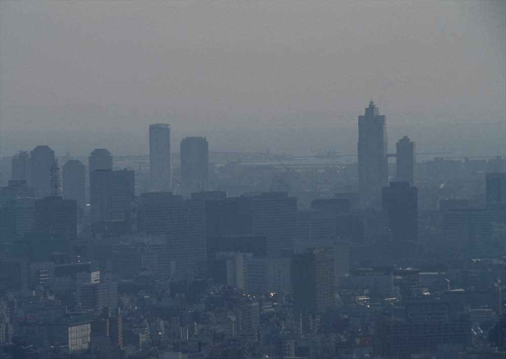 IMAGE_これは都市の風景を捉えた写真のようです。高層ビル群と海が見え、遠くには霧や曇りの影響で視界が少しぼやけています。具体的な場所はわかりませんが、都市部の風景であることが伺えます。