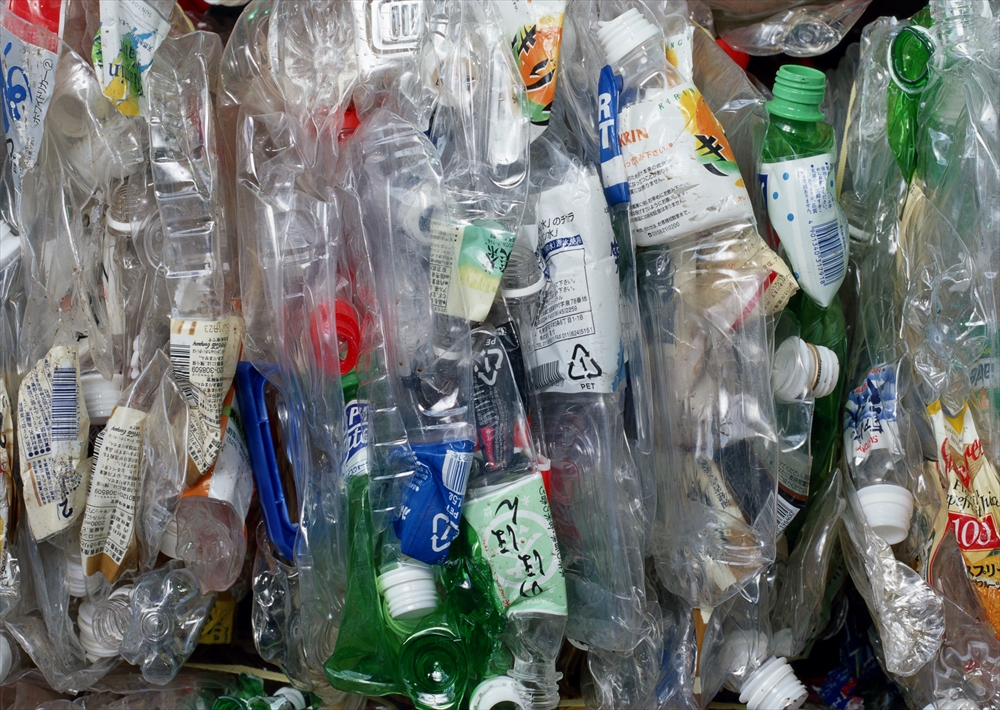 IMAGE_この写真は、廃棄されたプラスチック容器やボトルが積み重なっている様子を示しています。リサイクル可能なプラスチックごみが大量に集まっているシーンです。