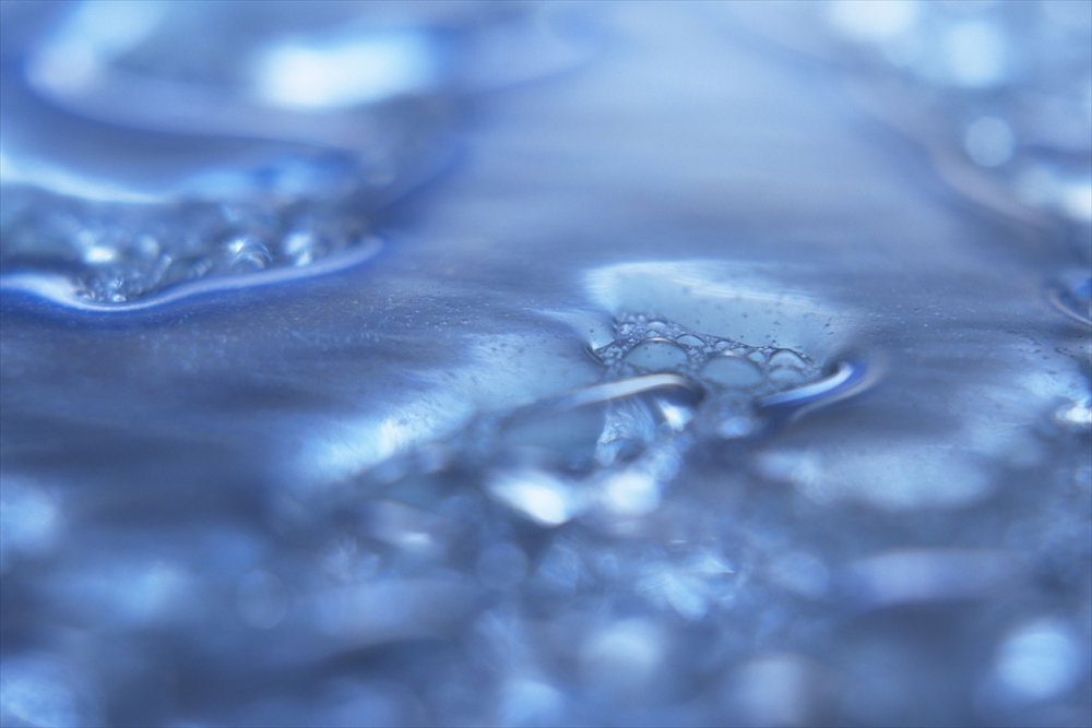 IMAGE_この写真は青い色調の水や液体のマクロ撮影のように見えます。水の中の気泡や波紋が映し出されており、抽象的で静かな印象を与えます。具体的には何を表しているのかは不明ですが、透明感や流動性を感じさせる画像です。