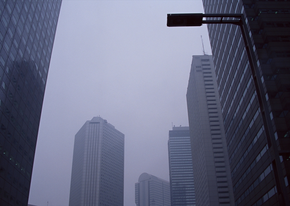 IMAGE_これは高層ビルが建ち並ぶ都市の風景を捉えた写真のようです。また、曇りや霧のような天候が感じられ、全体的に暗い雰囲気が漂っています。具体的な場所については分かりません。