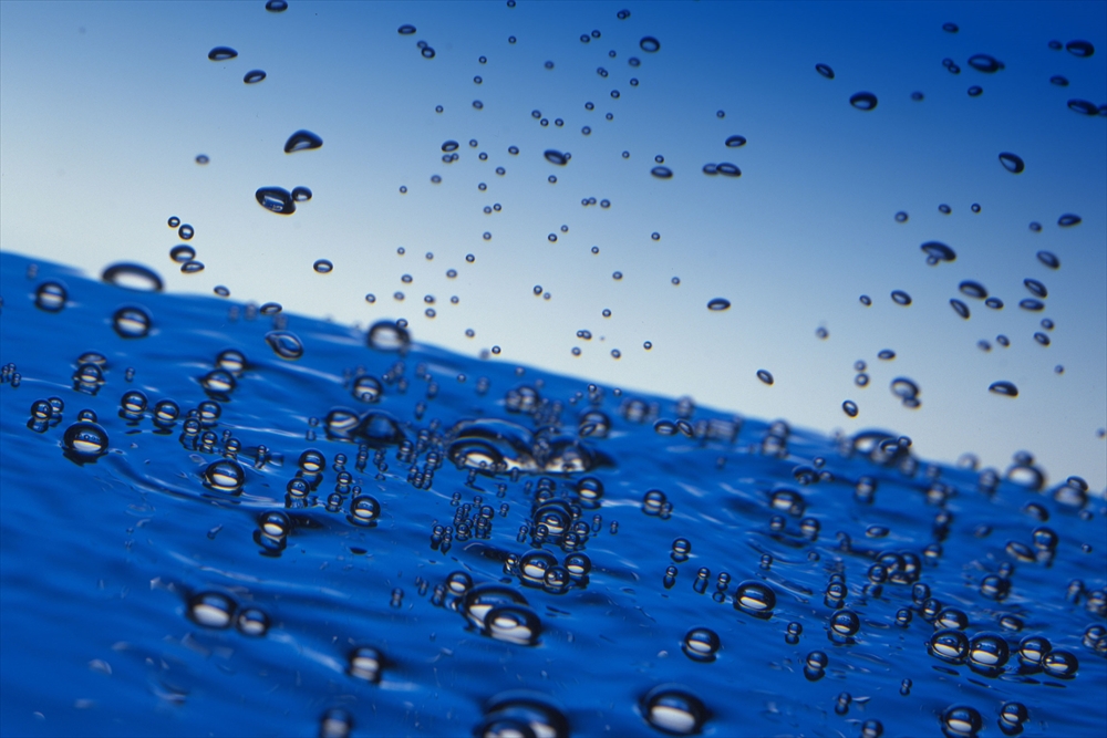 IMAGE_これは水面の上で水滴が跳ねている写真のようです。また、青い背景が水の深さや空間の印象を与えています。全体的に、清涼感や新鮮さを感じさせるイメージです。