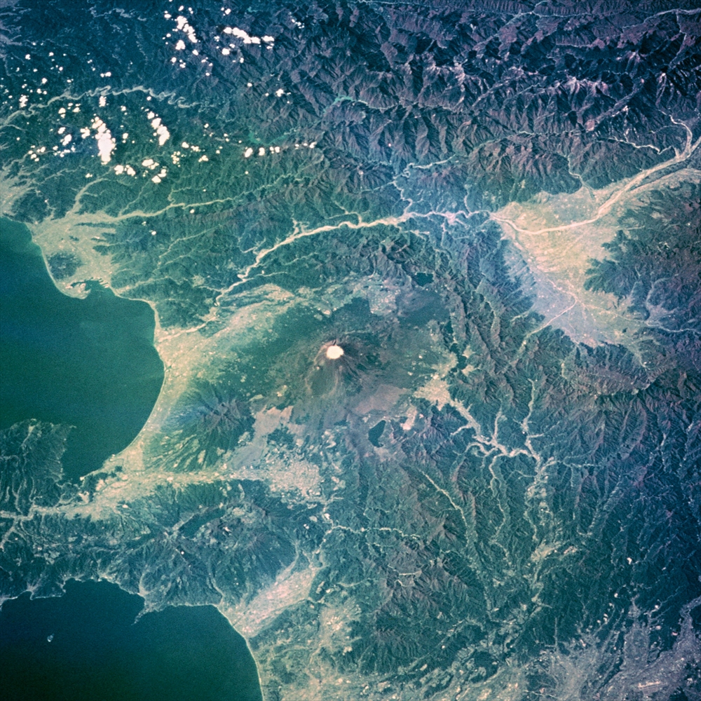 IMAGE_これは衛星から撮影された地球の写真のようです。中央には山が見え、その周りには土地や水域が広がっています。この山は富士山である可能性が高いです。画像からは日本の一部が捉えられているように見えます。