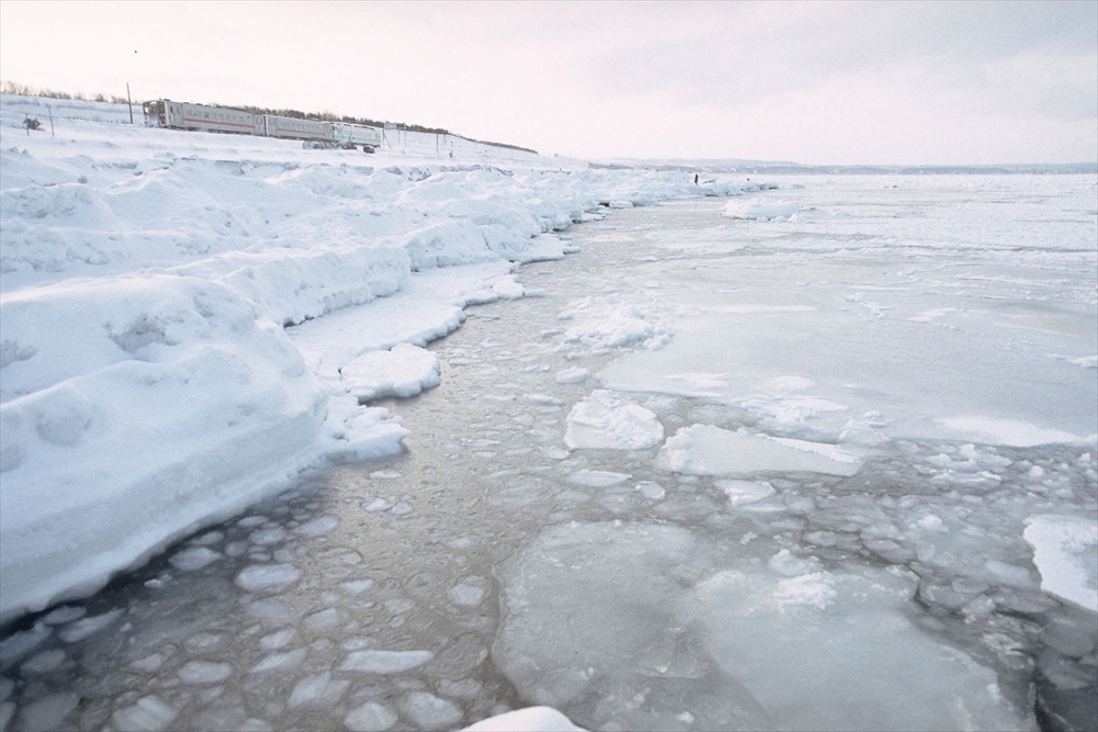 IMAGE_この写真は、雪や氷に覆われた風景を描いているようです。川や湖の氷、雪の積もった岸辺が見えます。寒冷地の冬の景色で、凍結した水面や雪のある環境を表現していると思われます。