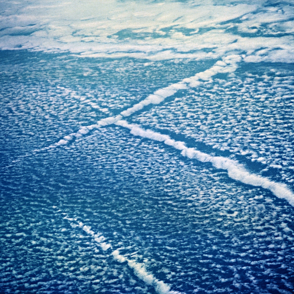 IMAGE_この写真は、上空から見た雲や海の様子を捉えたものです。雲の形状や配置が特徴的で、うねりやラインが見られます。これは航空機からの視点や海上の気象現象を映していると考えられます。具体的な場所や状況については判断できません。