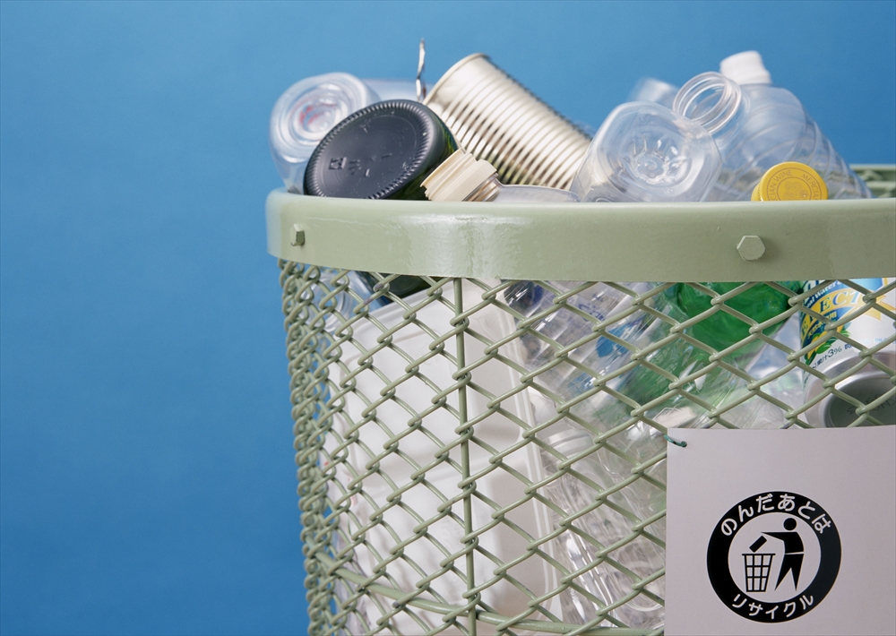 IMAGE_この写真は、ペットボトルや缶、プラスチックの容器などが入ったリサイクル用のゴミ箱を写しています。リサイクルを促進するためのサインも見えますね。背景は青色です。