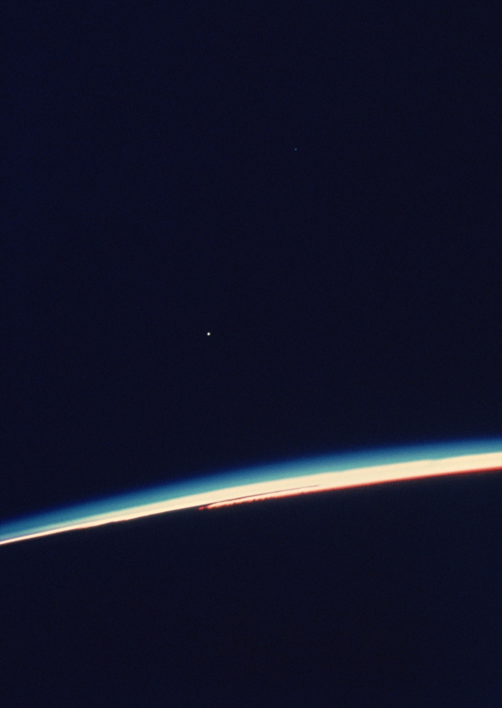 IMAGE_この写真は、地球の大気の境界面を捉えた宇宙からの画像のようです。地球の曲線と大気の薄い青い層が見え、空間には星や惑星が点在している可能性があります。宇宙からの地球の眺めを表現したものと思われます。