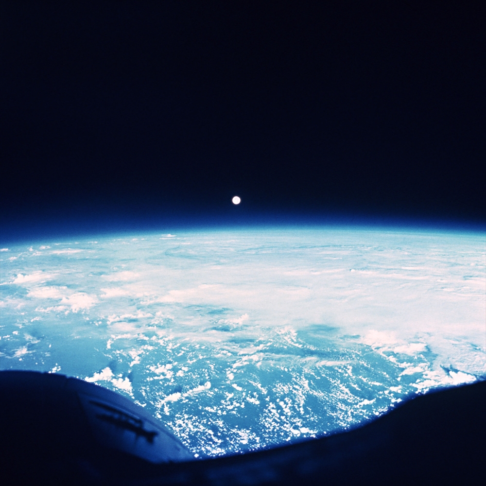 IMAGE_これは地球の宇宙からの写真で、地球の大気の境界や海、雲が見え、地平線の上にはおそらく太陽や月が見えていると思われます。宇宙からの壮大な視点を捉えたものです。