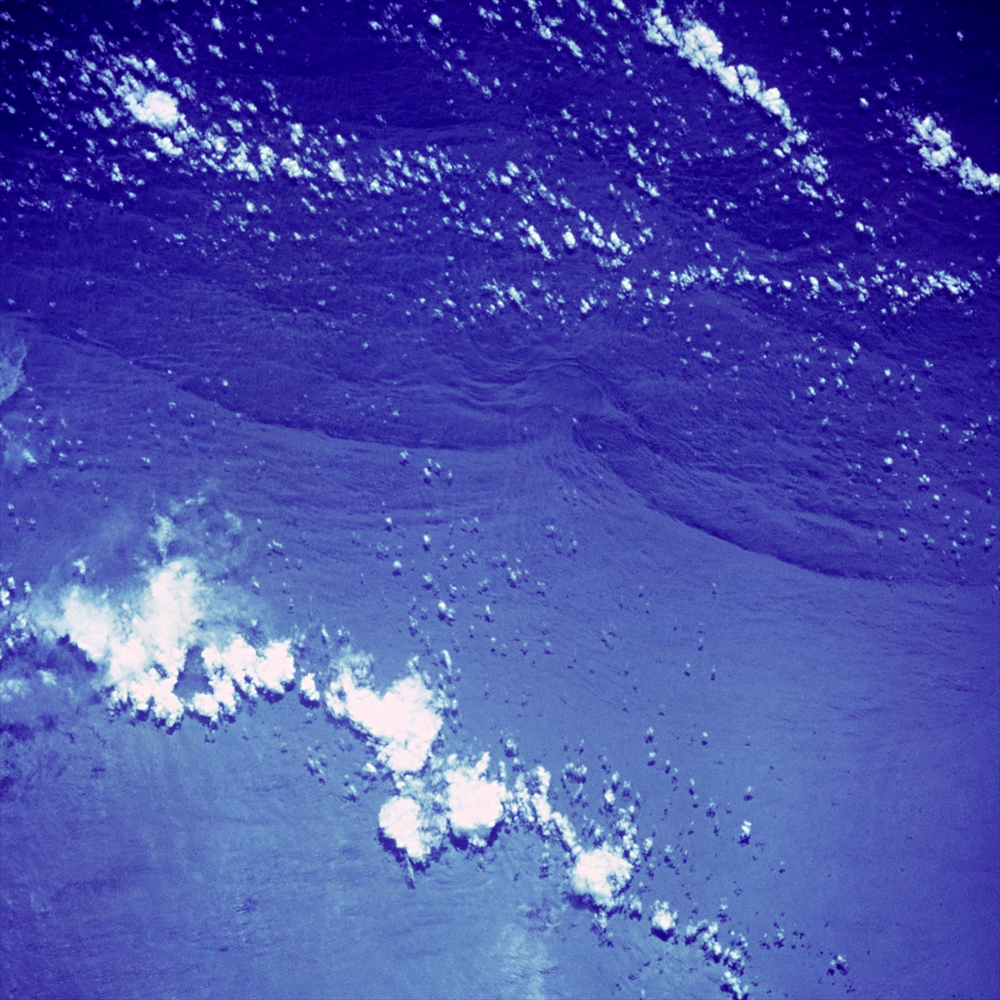 IMAGE_この写真は、宇宙からの地球の海や雲の様子を捉えたもののようです。特に、水面や雲が青いトーンで表現されており、大気の状態も示唆しているかもしれません。具体的な場所については、画像だけでは判断できません。