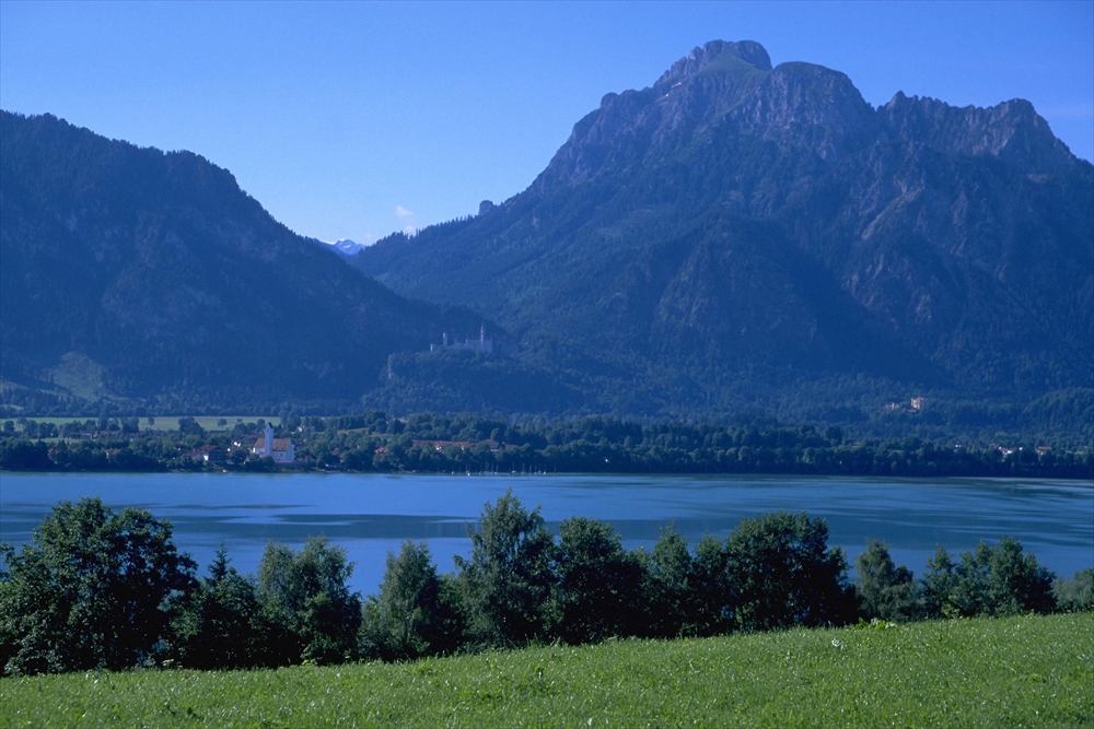 IMAGE_これは自然の風景を示す写真で、山と湖が写っています。青空のもと、緑豊かな草原や木々も見えます。おそらく、リラックスできる美しい風景や観光スポットの一部だと思われます。具体的な場所についてはわかりません。