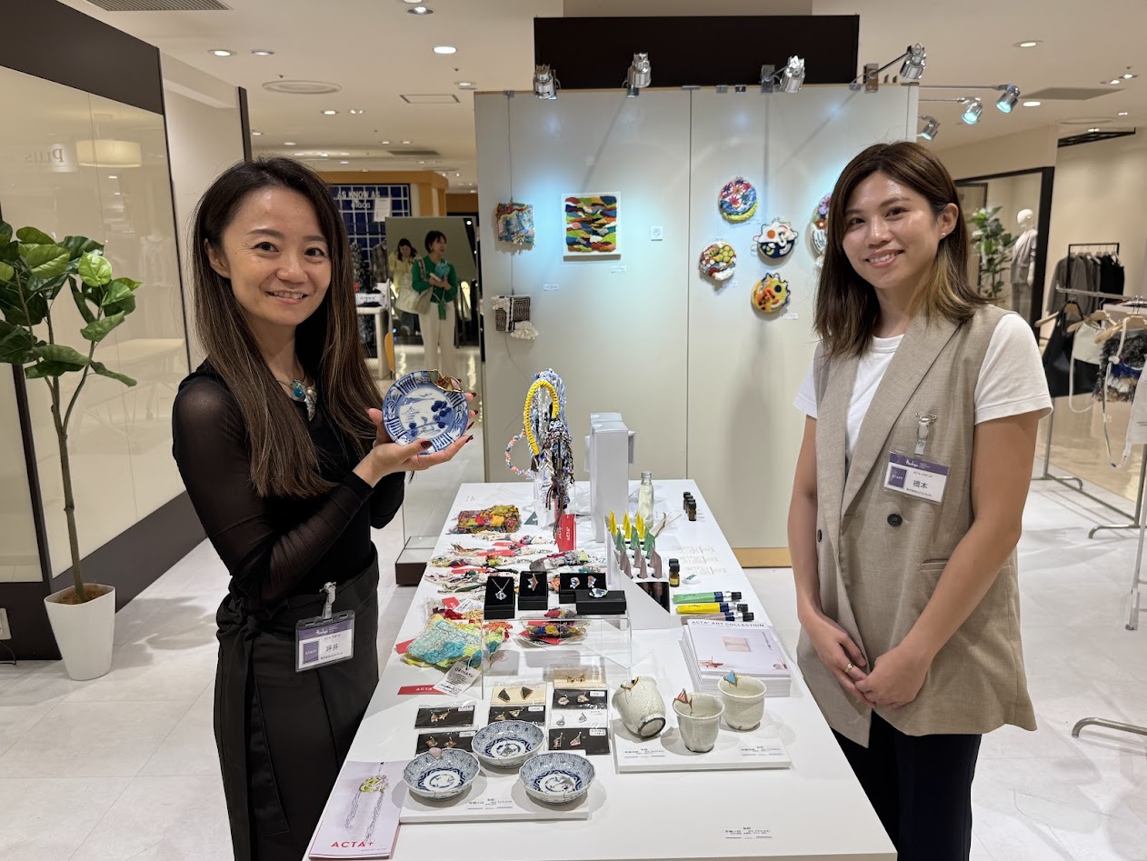 イベント会場で、作品を手にするアーティストの梨絵さん（左）と、ACTA PLUSの橋本希和子代表取締役